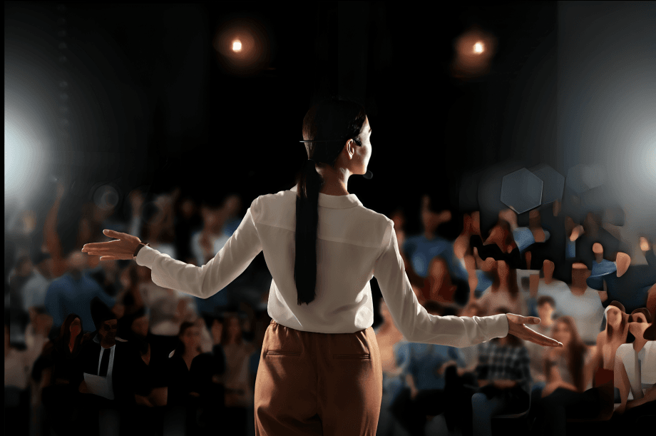 A woman speaking to a large, blurred audience on stage.