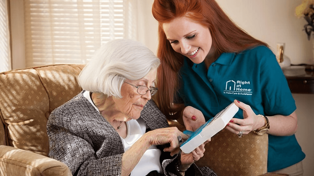 Caregiver assisting elderly woman with medication box.