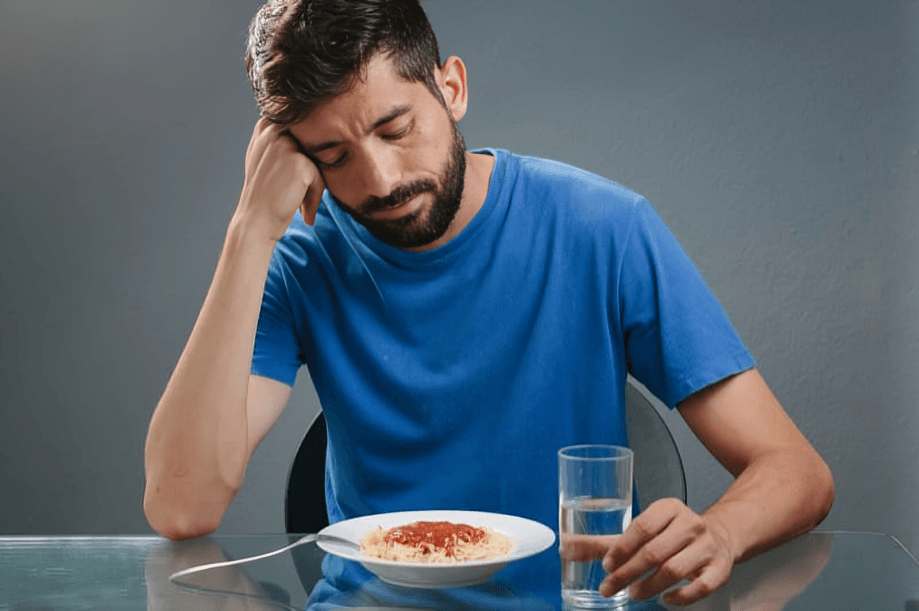 Tired man with spaghetti and water at a table.