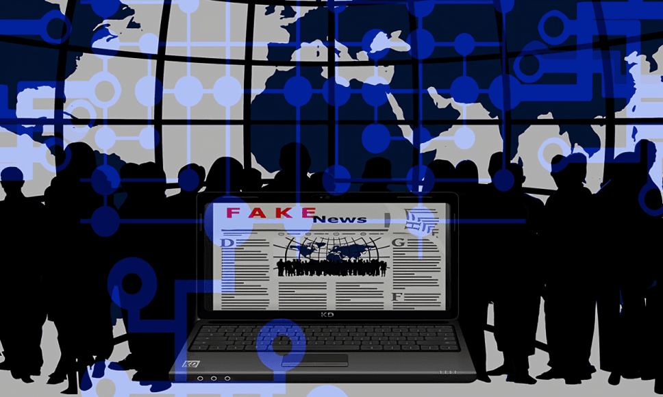 Laptop displays "Fake News" amidst a crowd and a global network.