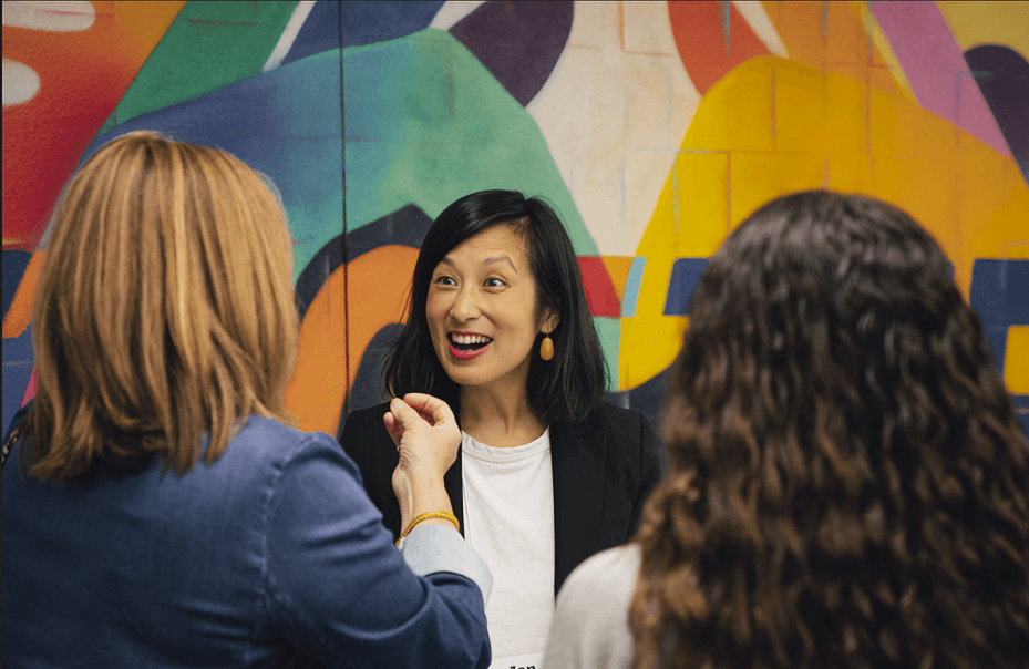 Three women in conversation against the colorful background.
