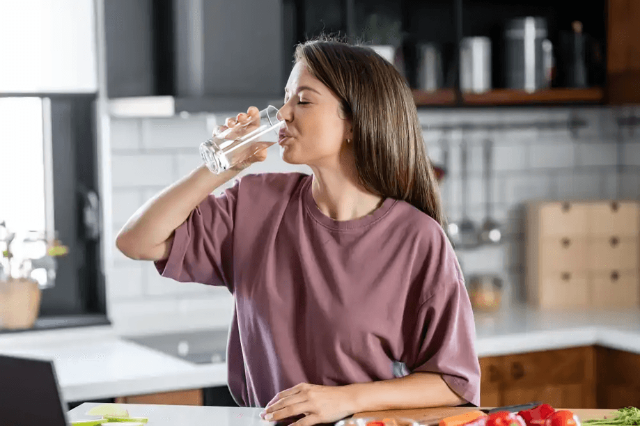 A person drinking water in a kitchen with a laptop.