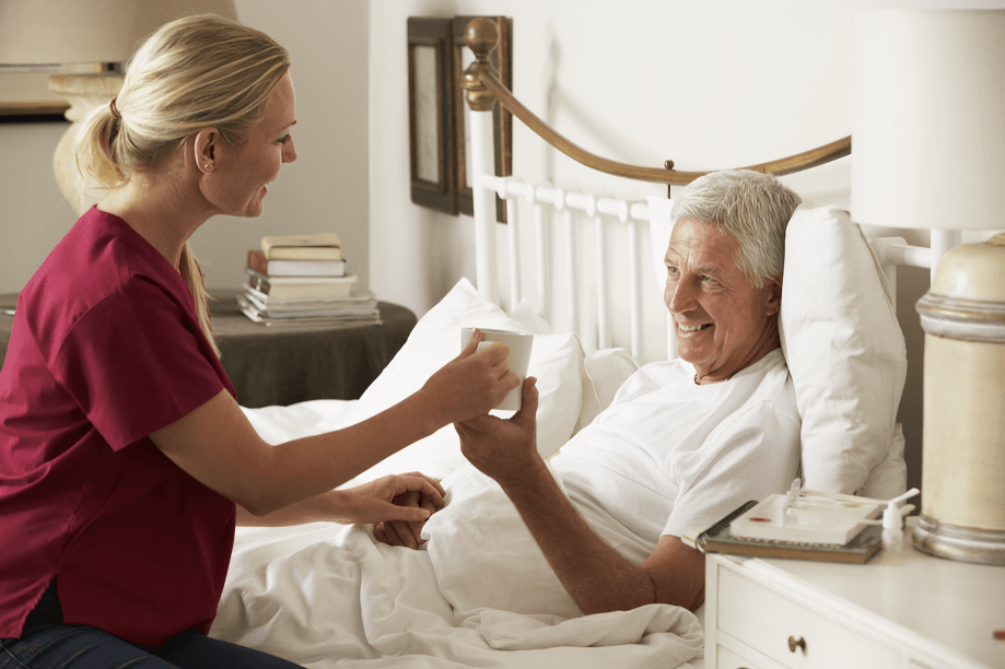 The caregiver, smiling, offers a drink to the senior man.