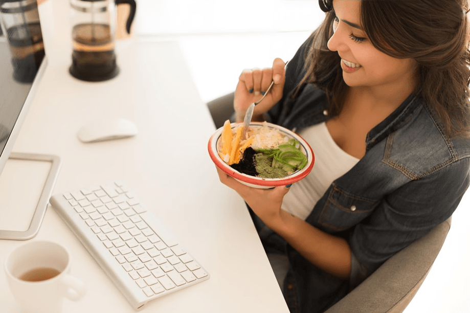 A smiling woman enjoys a healthy bowl at her desk.