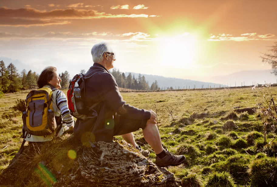 Elderly couple with backpacks enjoy the sunset mountain vista.