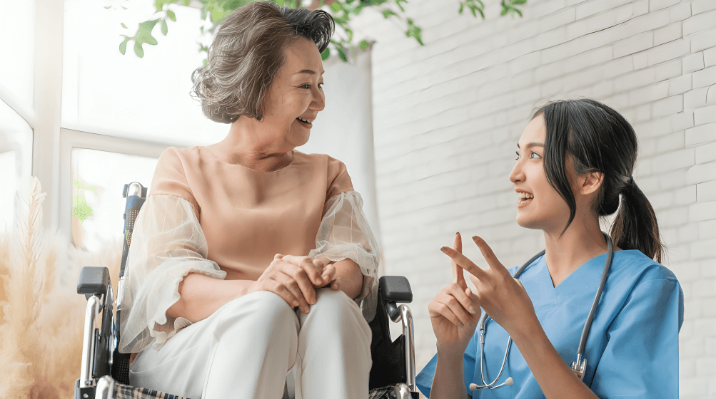 Smiling caregiver chats with senior in wheelchair.