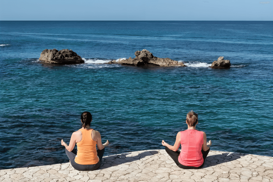 Two women meditating by the calm blue sea.