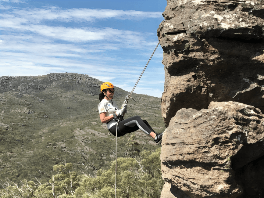 Woman rappelling down a rocky cliff face outdoors.