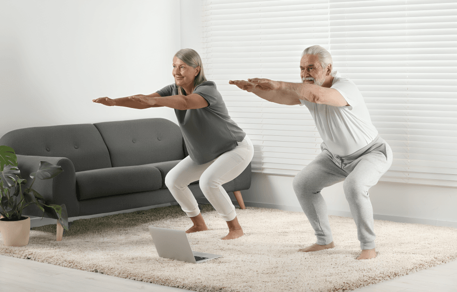 Two seniors squatting indoors while following a fitness video.