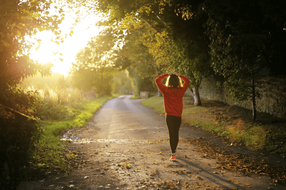 A woman stretches on a sunlit path lined with trees.
