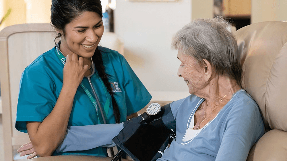 Nurse takes elderly woman's blood pressure, both smiling.