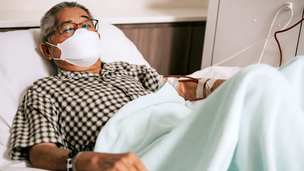 Elderly man with mask in hospital bed.