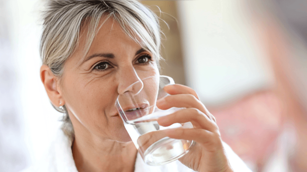 An older woman with grey hair drinking water.