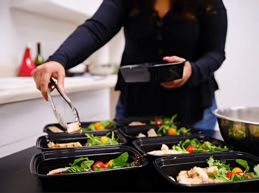 A person preparing meal prep containers with salad and chicken.