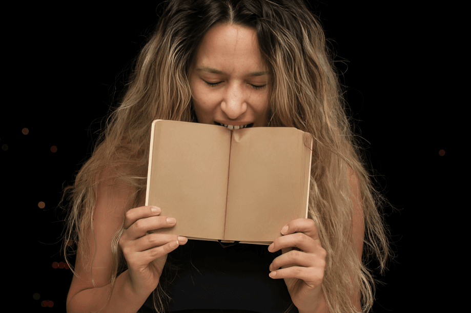 The woman appears to bite a small, open notebook intently.