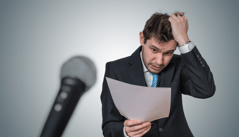Nervous speaker with notes and a microphone, looking stressed.