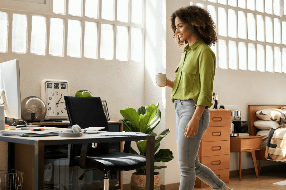 Woman with coffee walks past home office setup.
