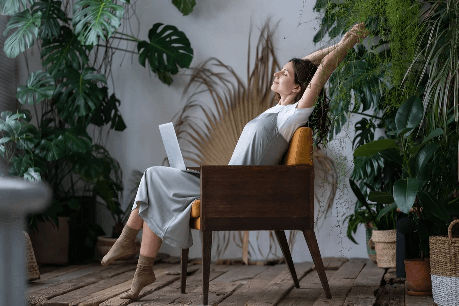 A woman relaxing in a chair surrounded by indoor plants.