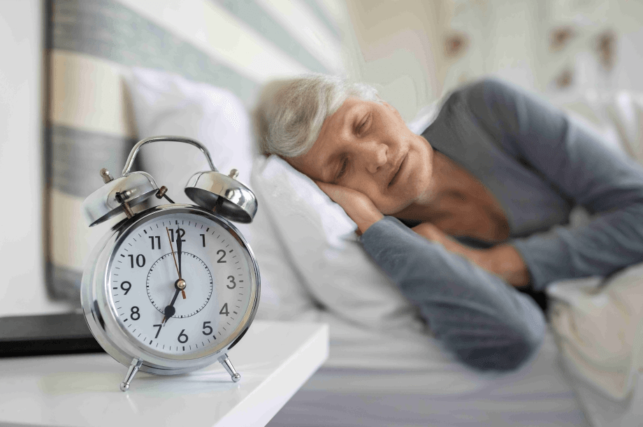 Alarm clock on nightstand with sleeping woman.