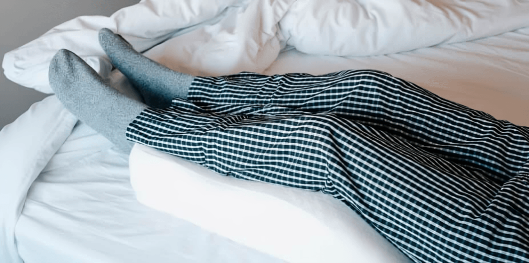 A person's legs elevated on a pillow in bed.