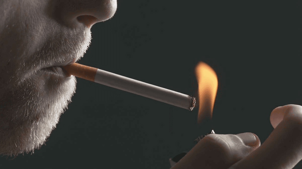 A man lighting a cigarette with a lighter, smoking.