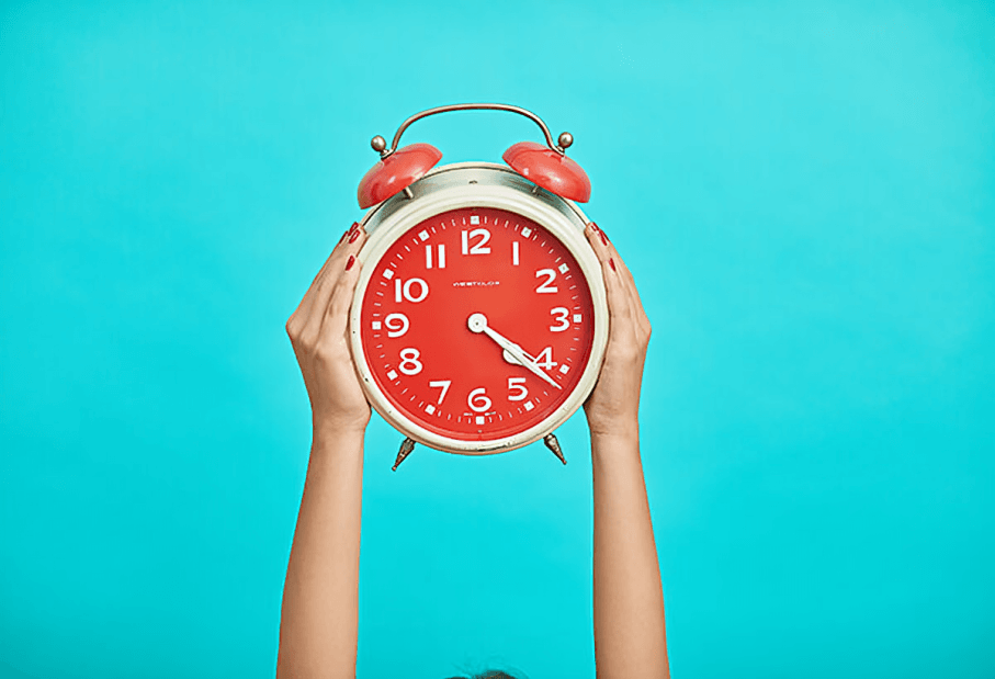 Hands holding a classic red alarm clock.