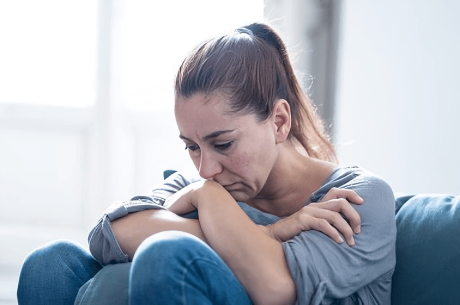 A woman appears sad and pensive on a couch.