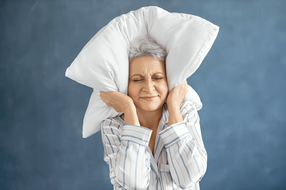 Elderly woman covering ears with a pillow.