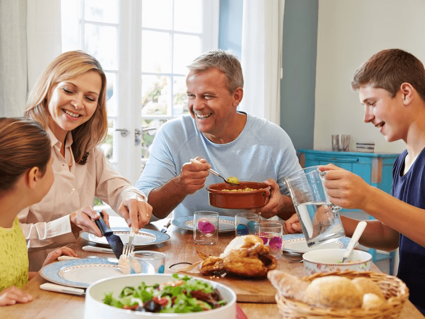 A family sharing a meal around a table, smiling and laughing.
