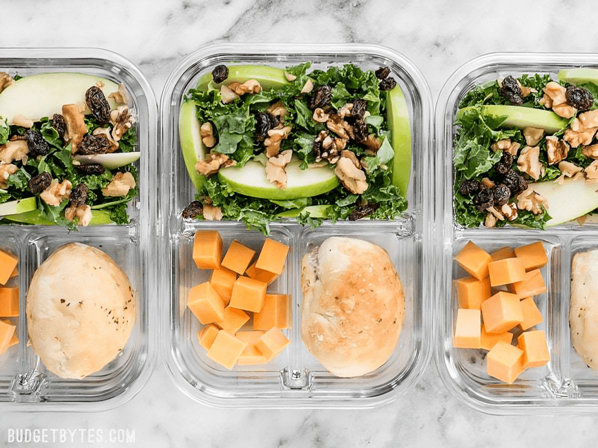 Three glass meal prep containers with salad, chicken, and cheese.