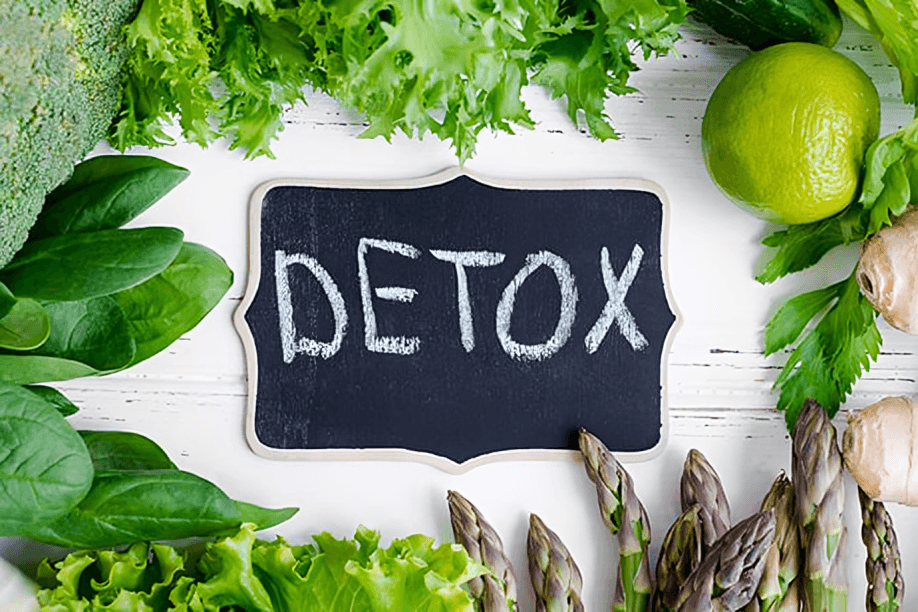 Detox sign surrounded by green vegetables on a white background.