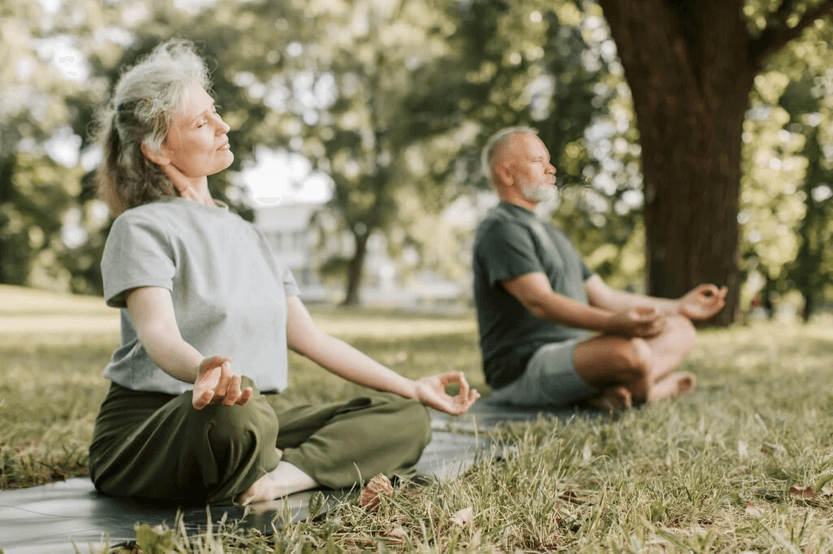 An older couple meditating outdoors in a park setting.