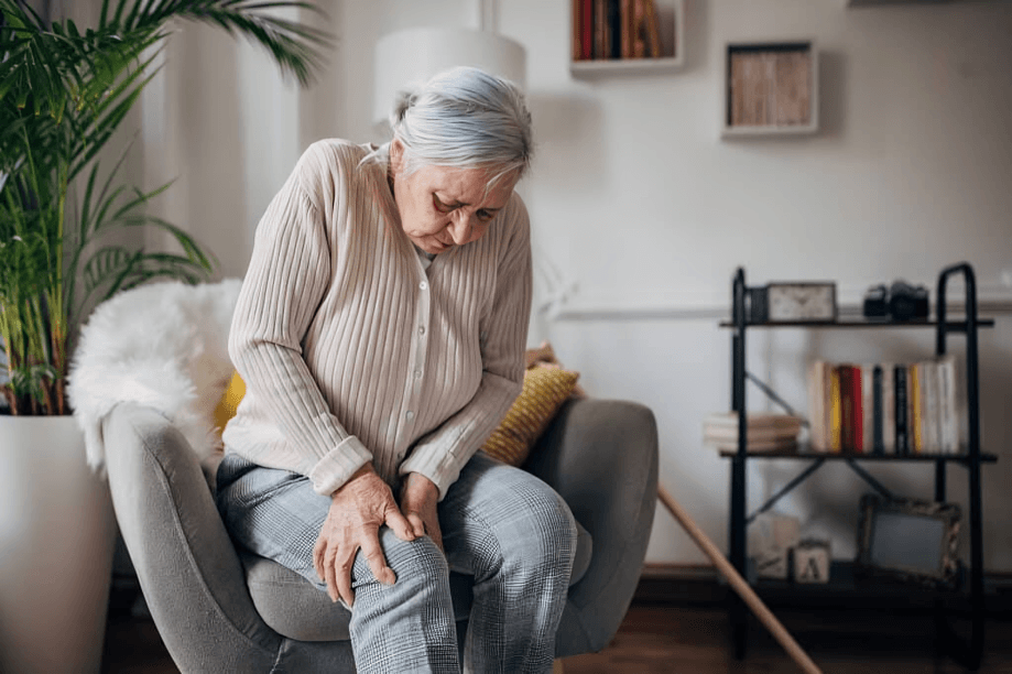 Elderly woman sitting, holding her painful knee.