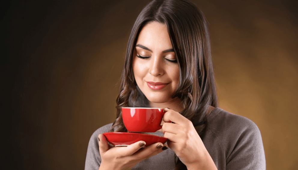 Woman in a gray shirt holding a red cup and saucer.
