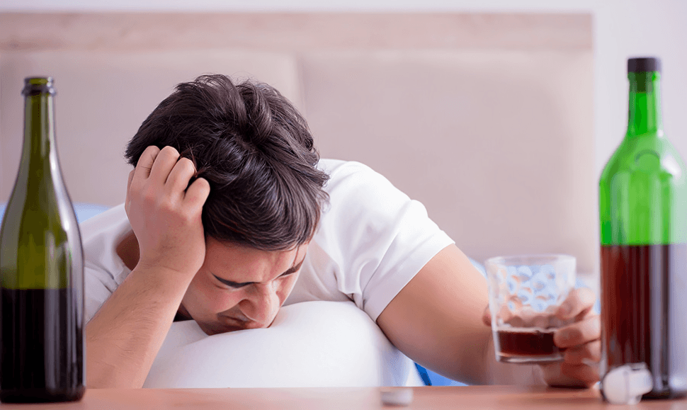 Man in bed with alcohol, possibly hungover.