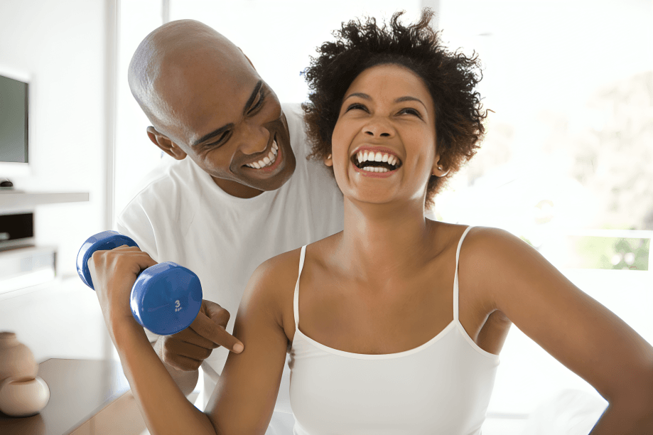A laughing couple, possibly African, exercising with a dumbbell.