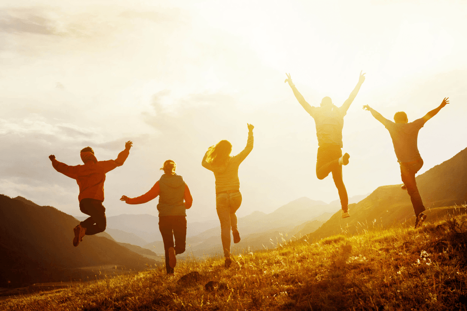 Silhouettes of five people joyfully jumping on a hill.