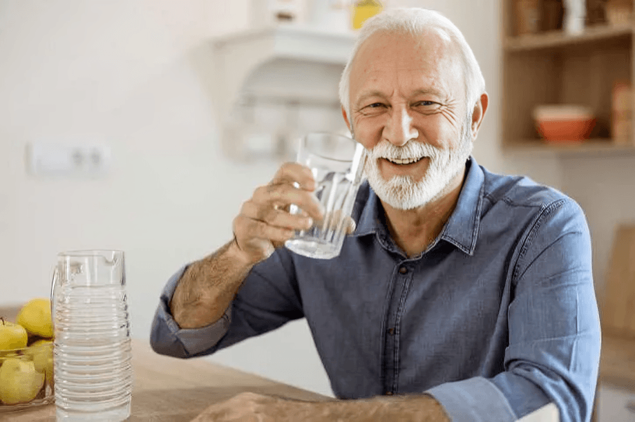 Smiling elderly man holding a glass of water.