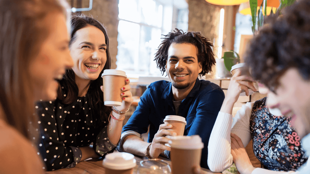 Smiling diverse friends enjoying coffee and conversation at a cafe.