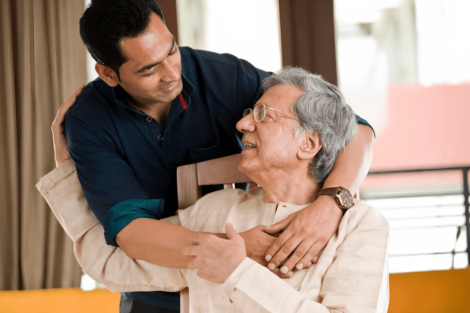 A man embracing an older man sitting in a chair.