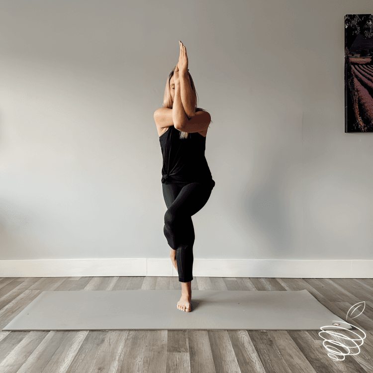A woman in Eagle yoga pose on a mat.