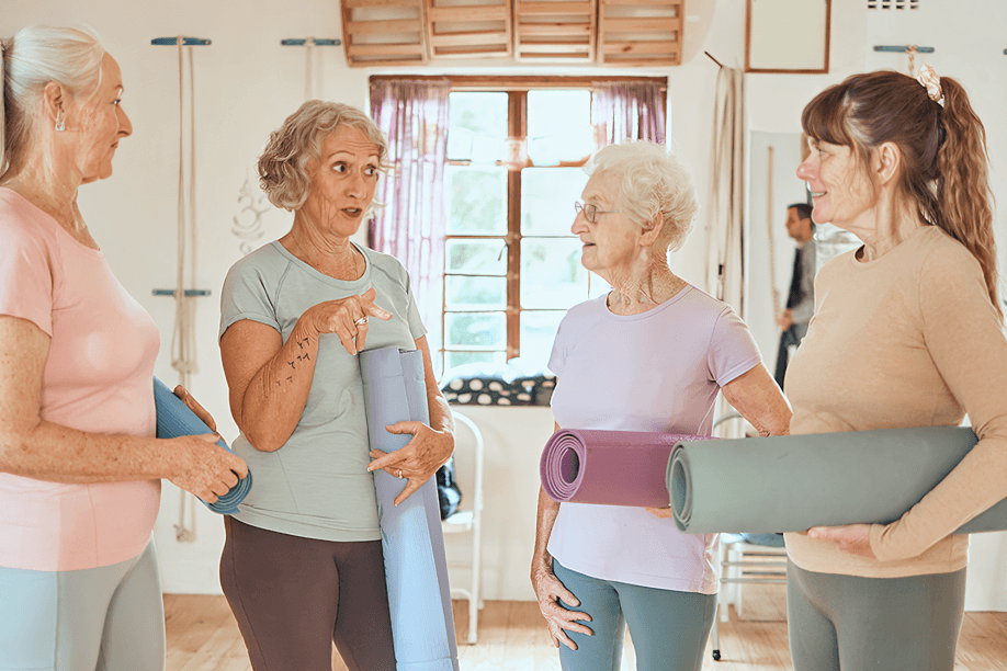 Four senior women with yoga mats chatting.