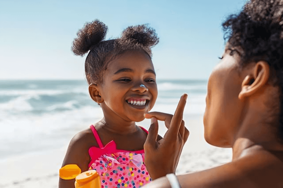 A mother applying sunscreen to her young daughter at the beach.