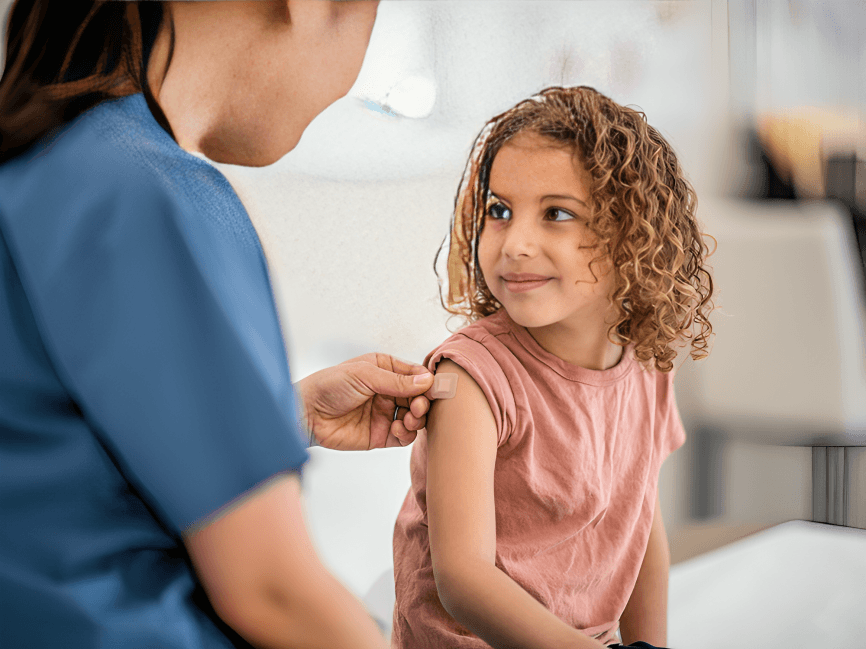 Young girl with curly hair receives vaccination from nurse.