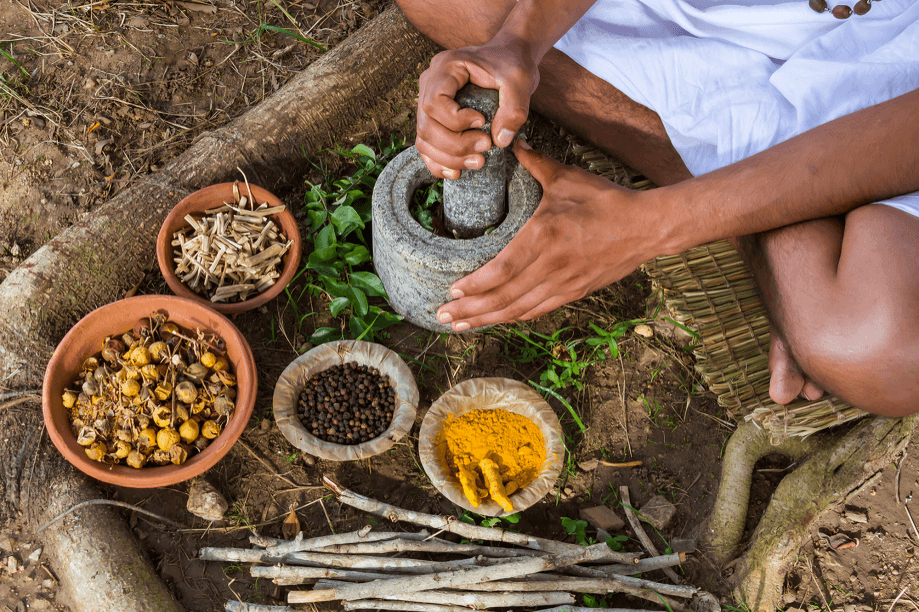 Hands grinding herbs with mortar and pestle outdoors.