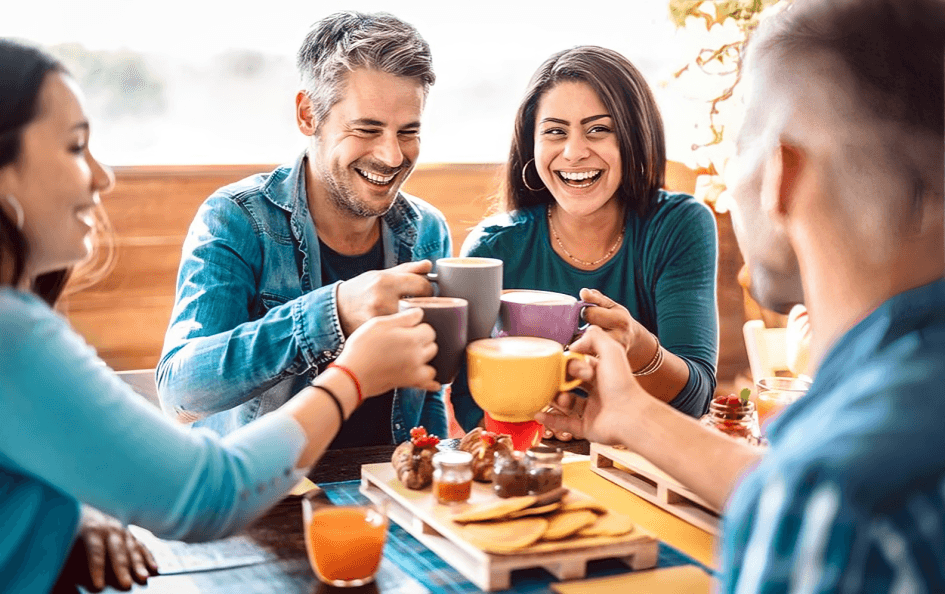 Four friends laughing and toasting with coffee cups.