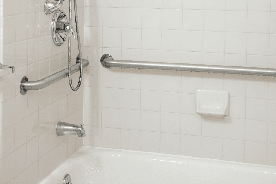 Bathroom with white tiles, tub, and grab bars.