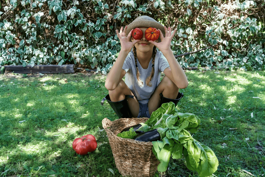 A person holds two tomatoes over their eyes outdoors.