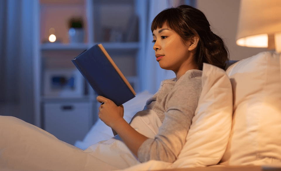 A person is reading a book in bed at night.