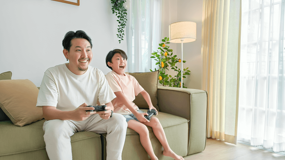 Father and child joyfully play video games on the sofa.